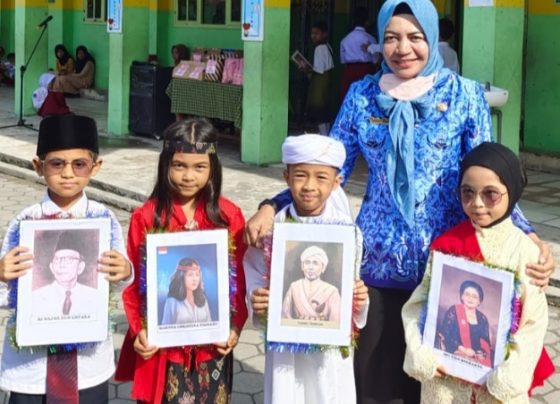 Siswa SDN 5 Baamang Hilir sambil membawa foto pahlawan yang wajahnya mereka tiru didampingi Kepsek Tuti Rahayu berpakaian warna biru