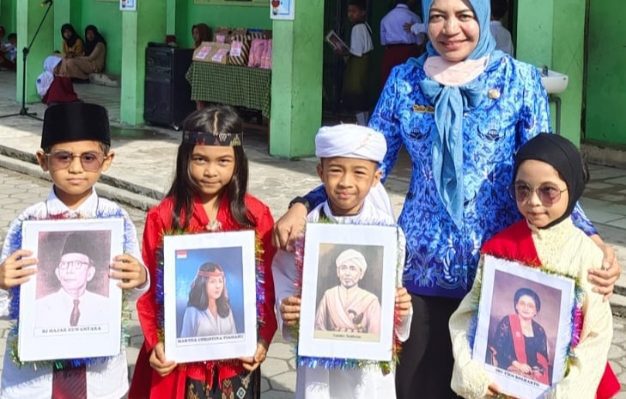 Siswa SDN 5 Baamang Hilir sambil membawa foto pahlawan yang wajahnya mereka tiru didampingi Kepsek Tuti Rahayu berpakaian warna biru