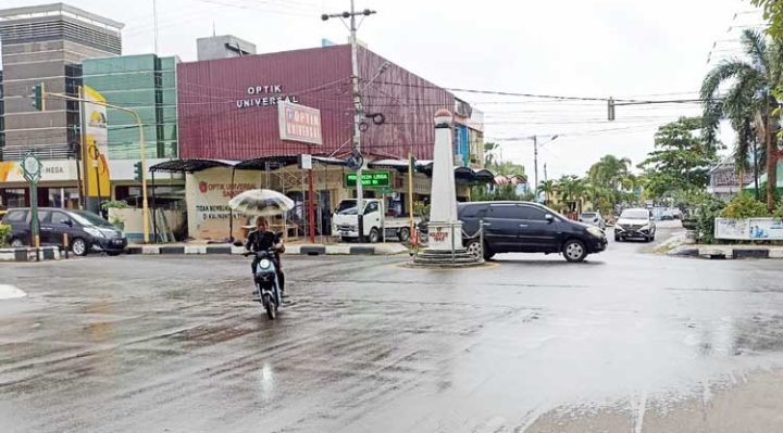 Pengguna sepeda listrik menembus hujan dengan membawa payung saat melintas di jalan perkotaan Sampit