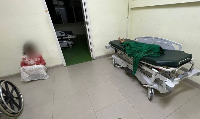 Tersangka pembunuhan terhadap anak kandung tersandar di rumah sakit dengan pakaian masih berlumuran darah, tampak mayat sang anak terbaring.