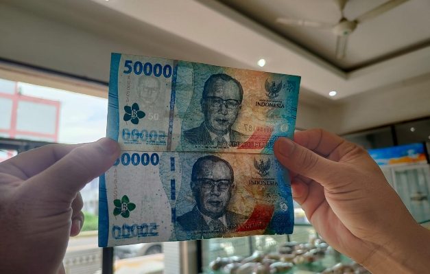 Gita saat menunjukan perbedaan uang palsu (di bawah) yang ia terima dan uang asli.