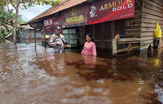 Seorang anggota Polri saat berbincang dengan warga di Desa Sei Ubar Mandiri, yang rumahnya terendam banjir, Minggu, 18 Februari 2023.