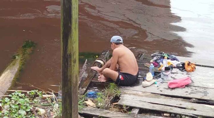 Aktivitas warga mandi dan mencuci pakaian di Sungai Mentaya sekitar lokasi pencemaran limbah minyak yang diduga dibuang secara sengaja oleh anak buah kapal yang tambat di sekitar lokasi tersebut.
