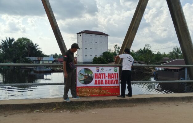 isi I Edy Mashami saat memasang spanduk peringayan keberadaan buaya di atas jembatan Sungai Sampit, Kecamatan Mentaya Hilir Utara, Minggu, 4 Mei 2025.