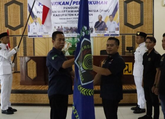 Ketua PWI Kalteng Jainal memberikan bendera PWI kepada Ketua PWI Katingan Ancu pada konferensi di Aula Dinas PUPR, Kamis, 19 Juni 2025